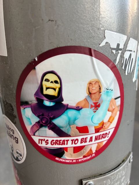Runder Aufkleber mit Skeletor und He-Man Actionfiguren. Skeletor hebt den Arm, darunter steht in englischer Sprache: „IT’S GREAT TO BE A NERD!”. 