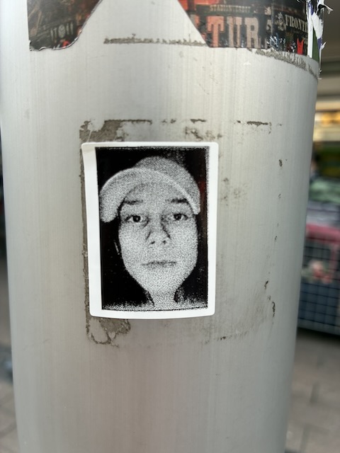 Schwarz-weißes Bild einer Person in seitlicher Ansicht mit heller Mütze oder Kapuze. Der Rest des Gesichtes und Hintergrunds sind stark verrauscht und stilisiert.