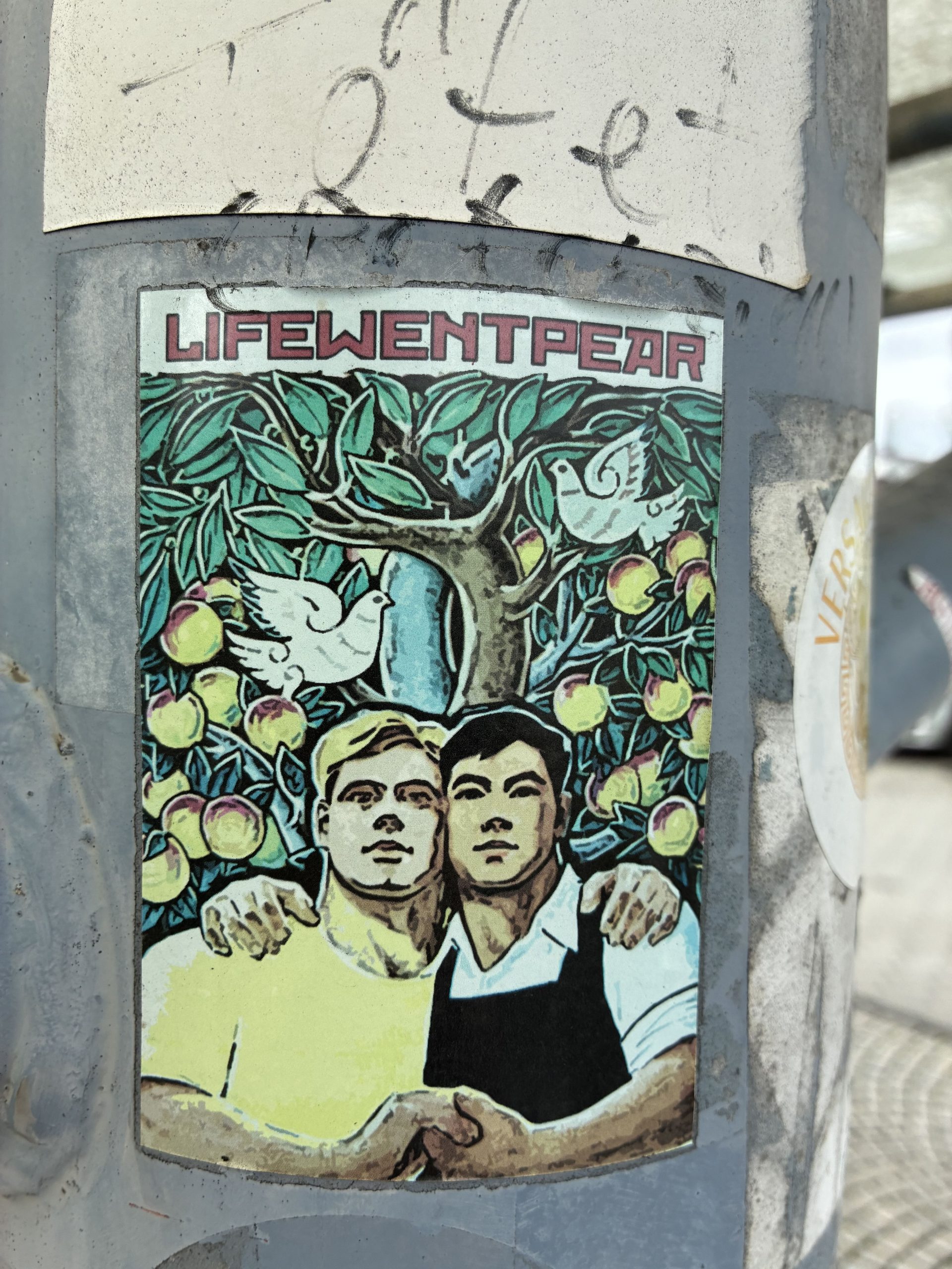 Rechteckiger, farbiger Sticker auf einem grauen Mast. Oben steht in rosa Großbuchstaben „LIFEWENTPEAR“. Darunter eine Illustration: Zwei junge Männer stehen eng beieinander, die Arme umeinandergelegt. Hinter ihnen ein dichter Birnbaum mit vielen gelb-grünen Früchten und zwei weißen Tauben zwischen den Ästen. Kräftige Grün-, Gelb- und Blautöne dominieren das Bild.