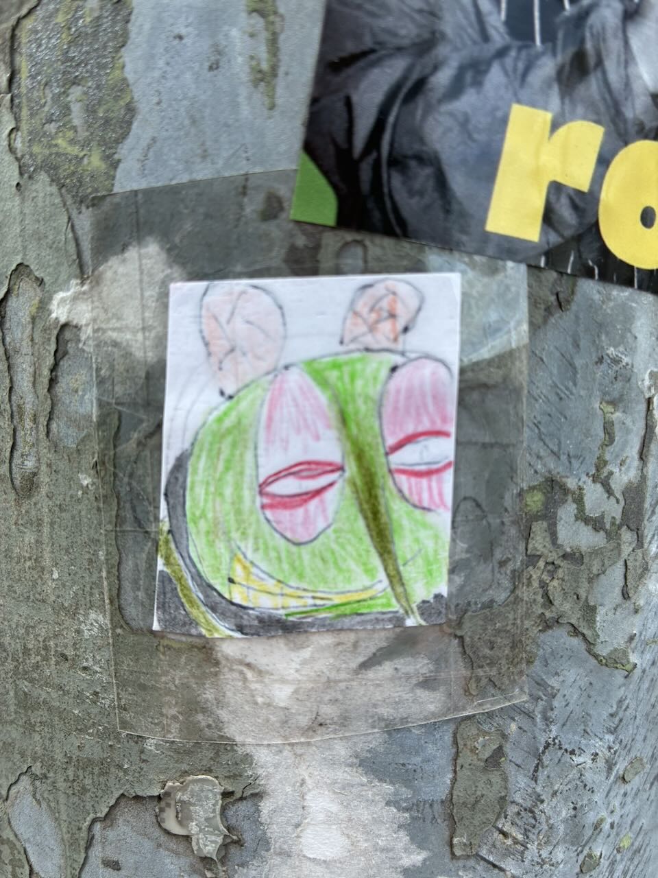 Sticker auf einer rauen, grauen Oberfläche. Das Motiv zeigt ein stilisiertes Insektengesicht mit großen, roten Augen, grünem Kopf und langen, grünen Fühlern. Der Sticker wirkt handgezeichnet und ist leicht schief geklebt.